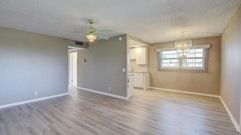 interior space featuring ceiling fan with notable chandelier, light hardwood / wood-style flooring, and a textured ceiling