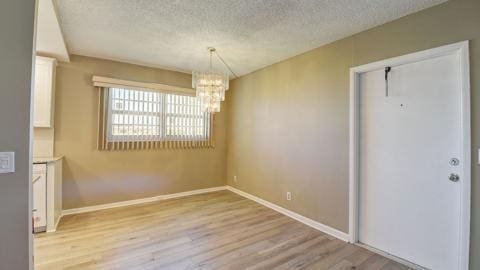 unfurnished dining area featuring an inviting chandelier, light hardwood / wood-style floors, and a textured ceiling