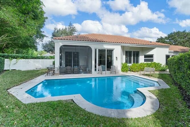 rear view of property featuring a lawn, a sunroom, and a patio