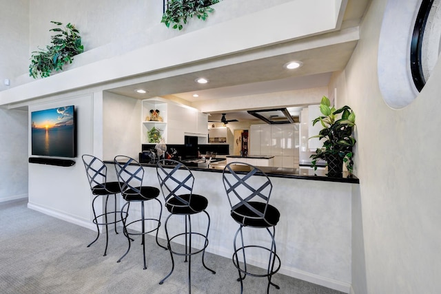 kitchen with light colored carpet, kitchen peninsula, white cabinetry, and a kitchen bar