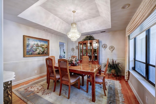 dining area with an inviting chandelier, hardwood / wood-style floors, and a raised ceiling