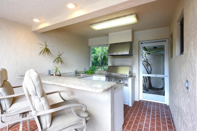 kitchen featuring sink, wall chimney range hood, kitchen peninsula, and a breakfast bar area