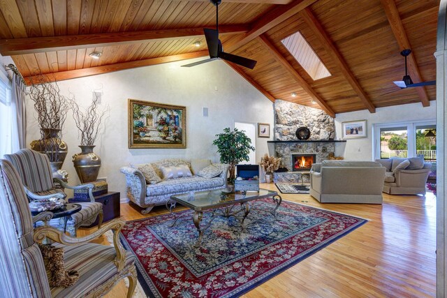 living room featuring wood ceiling, ceiling fan, vaulted ceiling with skylight, a fireplace, and light hardwood / wood-style flooring