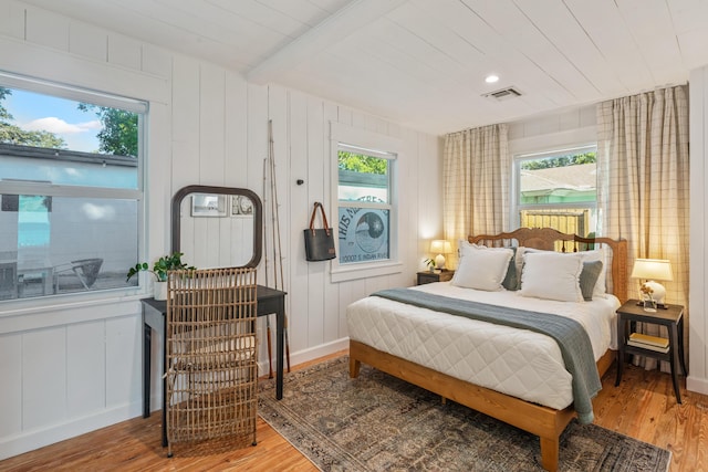 bedroom with beamed ceiling, wood-type flooring, and multiple windows