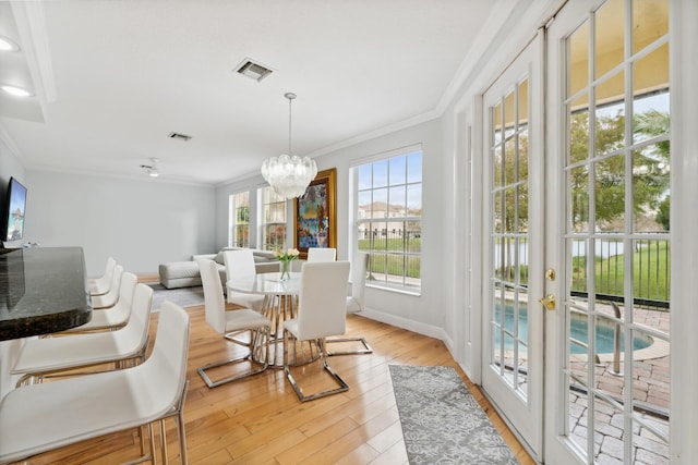 dining area featuring light hardwood / wood-style flooring, crown molding, french doors, and an inviting chandelier