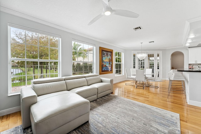 living room with ceiling fan with notable chandelier, plenty of natural light, crown molding, and light wood-type flooring