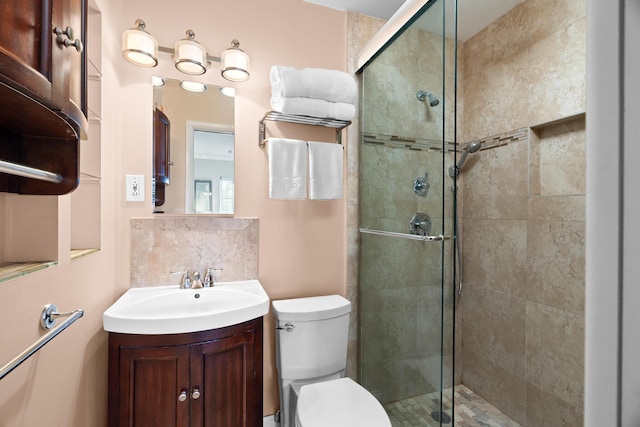 bathroom featuring vanity, toilet, a shower with door, and decorative backsplash