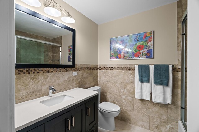 bathroom with tile walls, toilet, a tile shower, vanity, and tile patterned floors