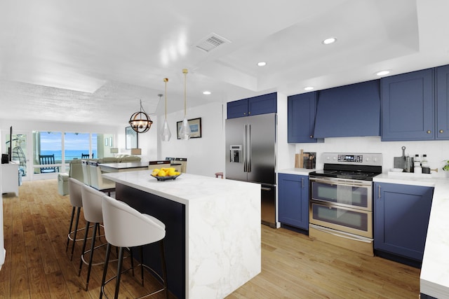 kitchen featuring light stone counters, ventilation hood, stainless steel appliances, blue cabinetry, and hanging light fixtures