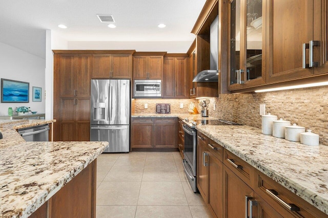 kitchen with light stone countertops, wall chimney range hood, decorative backsplash, light tile patterned floors, and appliances with stainless steel finishes