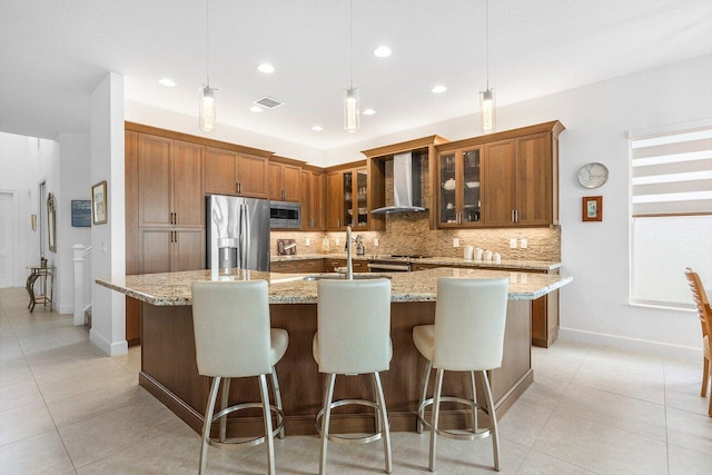 kitchen featuring a kitchen island with sink, pendant lighting, wall chimney range hood, and appliances with stainless steel finishes