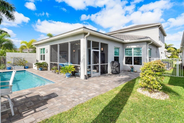 rear view of property featuring a lawn, a patio area, a sunroom, and a fenced in pool