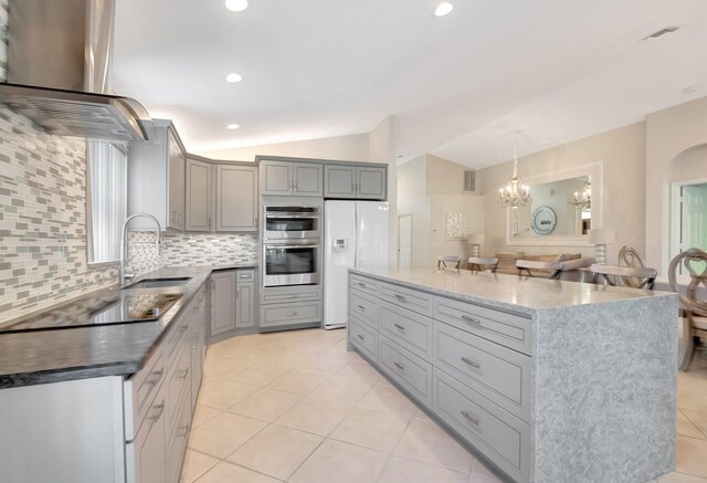 kitchen featuring tasteful backsplash, vaulted ceiling, wall chimney range hood, gray cabinets, and white fridge with ice dispenser