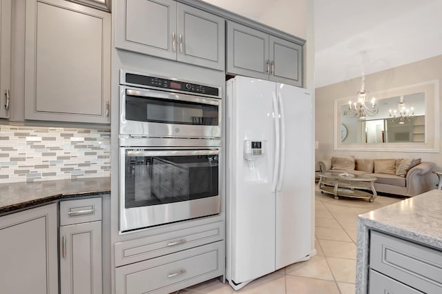 kitchen with backsplash, dark stone counters, gray cabinetry, double oven, and white refrigerator with ice dispenser