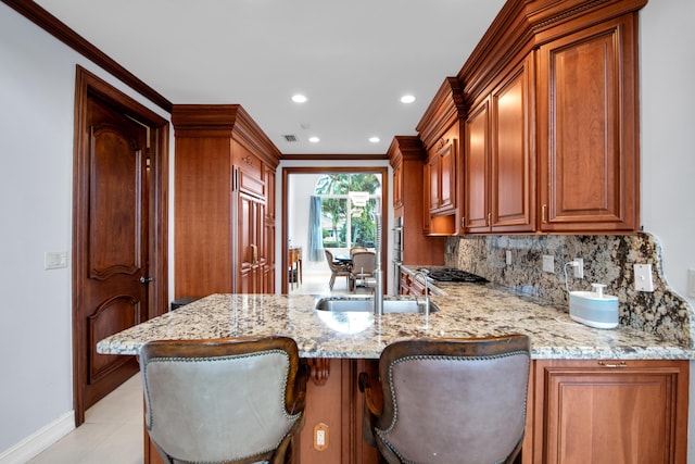 kitchen featuring a breakfast bar, kitchen peninsula, light stone counters, and sink