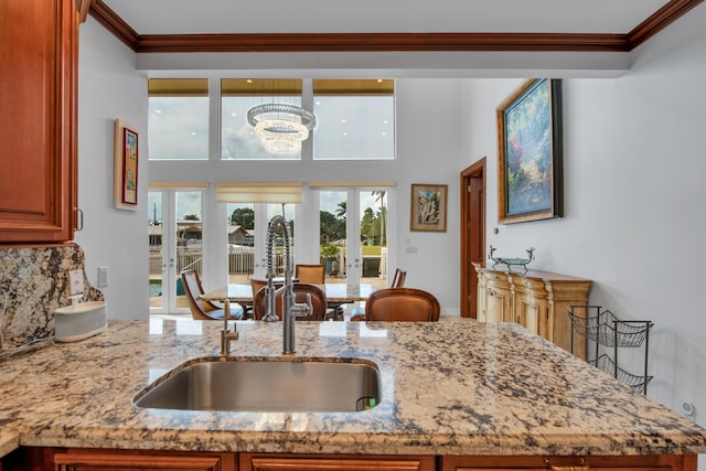 kitchen with french doors, light stone counters, ornamental molding, and sink