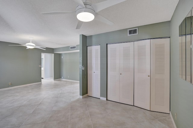 unfurnished bedroom with ceiling fan, a textured ceiling, and multiple closets