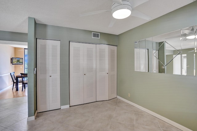 bedroom featuring ceiling fan, light tile patterned floors, and two closets