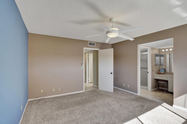 unfurnished bedroom with light carpet, a textured ceiling, ensuite bathroom, and ceiling fan