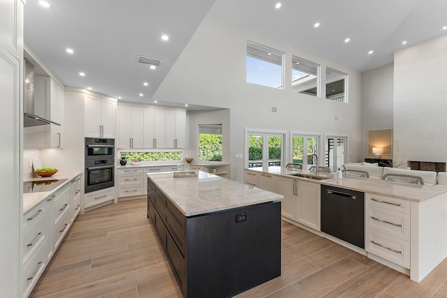 kitchen featuring light stone counters, a large island with sink, white cabinets, and black appliances