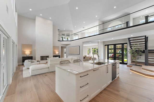 kitchen featuring light stone countertops, white cabinets, a center island with sink, and a towering ceiling