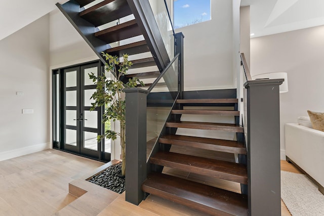 stairway with french doors, a towering ceiling, and hardwood / wood-style flooring