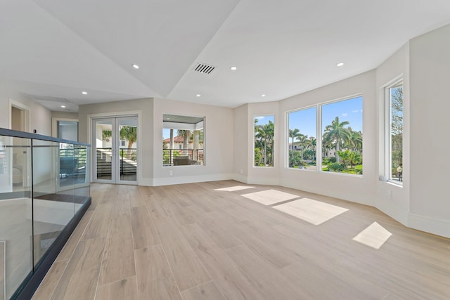 unfurnished room featuring lofted ceiling, french doors, plenty of natural light, and light hardwood / wood-style floors