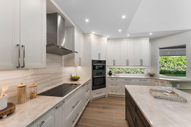 kitchen featuring white cabinetry, wall chimney range hood, black electric stovetop, double oven, and light wood-type flooring