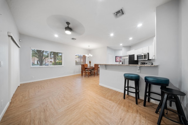 kitchen with white cabinetry, light stone countertops, light parquet flooring, ceiling fan with notable chandelier, and appliances with stainless steel finishes