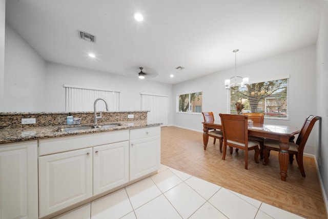 kitchen with white cabinets, ceiling fan with notable chandelier, dark stone countertops, light tile patterned floors, and decorative light fixtures