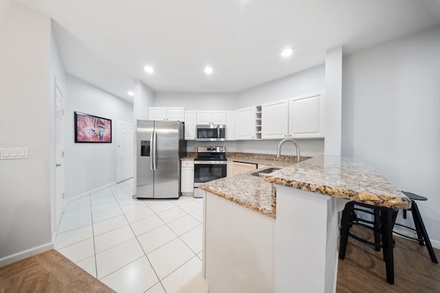 kitchen with kitchen peninsula, stainless steel appliances, sink, white cabinets, and light tile patterned flooring