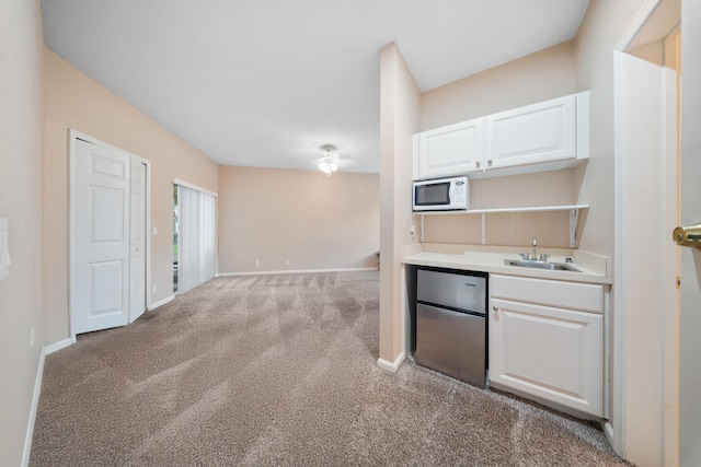 kitchen with carpet floors, sink, white cabinets, and fridge