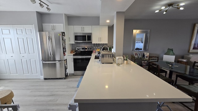 kitchen featuring kitchen peninsula, decorative backsplash, a notable chandelier, white cabinetry, and stainless steel appliances