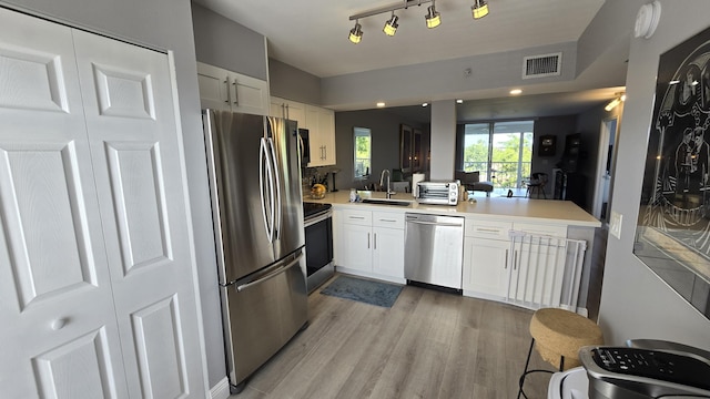 kitchen with sink, stainless steel appliances, kitchen peninsula, white cabinets, and light wood-type flooring