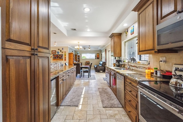 kitchen with backsplash, sink, hanging light fixtures, light stone countertops, and stainless steel appliances