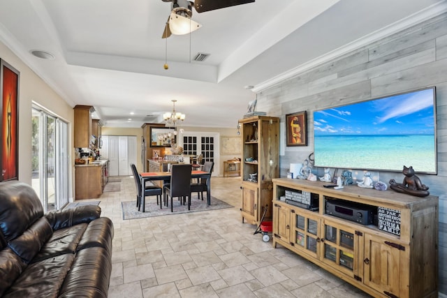 living room with a raised ceiling, wooden walls, and ceiling fan with notable chandelier