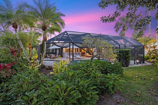 back house at dusk featuring a patio and glass enclosure