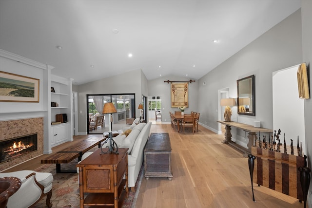 living room featuring light hardwood / wood-style floors, a tile fireplace, vaulted ceiling, and built in features