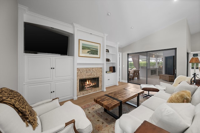 living room with a tiled fireplace, built in features, vaulted ceiling, and hardwood / wood-style floors