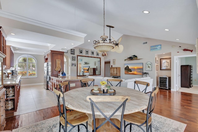 dining room with sink, wood-type flooring, ornamental molding, and vaulted ceiling