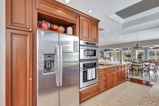 kitchen with a raised ceiling, crown molding, decorative light fixtures, light tile patterned floors, and appliances with stainless steel finishes