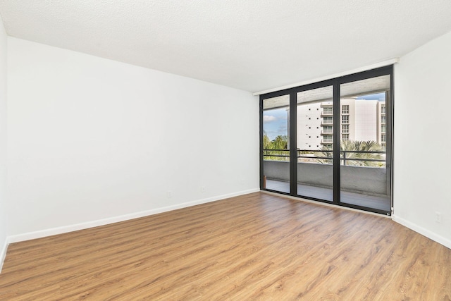 unfurnished room with a textured ceiling, light wood-type flooring, and a wall of windows