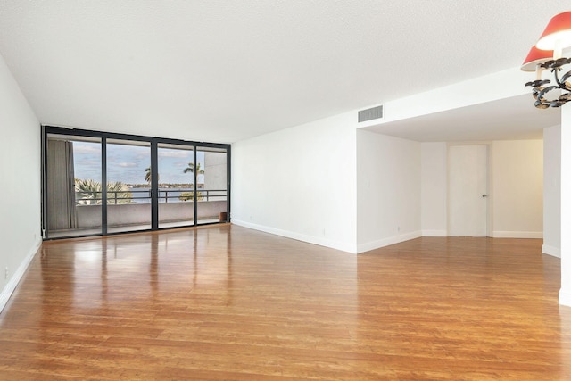 empty room with floor to ceiling windows, a textured ceiling, and light wood-type flooring