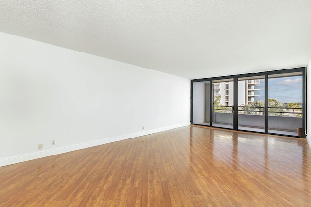 spare room with wood-type flooring, a textured ceiling, and a wall of windows