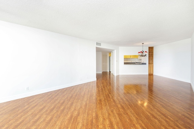 spare room featuring a chandelier, hardwood / wood-style floors, and a textured ceiling