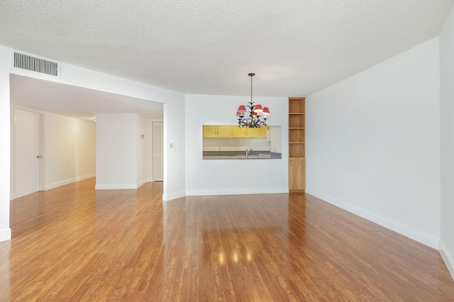 unfurnished room featuring a textured ceiling, sink, light hardwood / wood-style flooring, and a chandelier