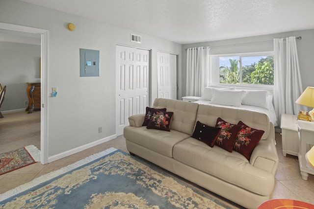 tiled living room featuring electric panel, visible vents, a textured ceiling, and baseboards