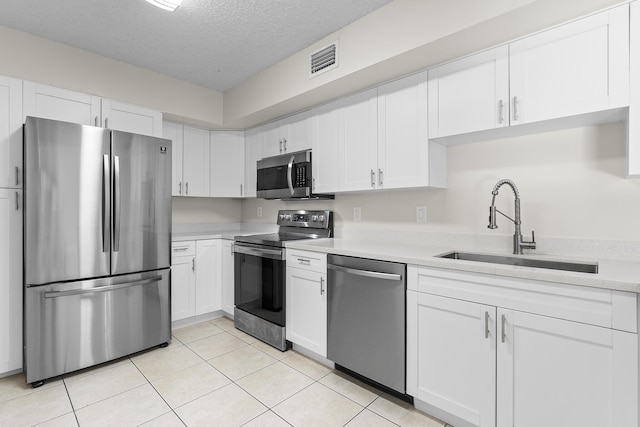 kitchen with appliances with stainless steel finishes, a textured ceiling, sink, white cabinetry, and light tile patterned flooring