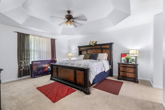 carpeted bedroom with a raised ceiling and ceiling fan