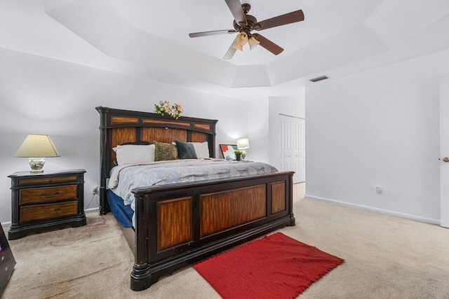 bedroom with a tray ceiling, ceiling fan, a closet, and light carpet